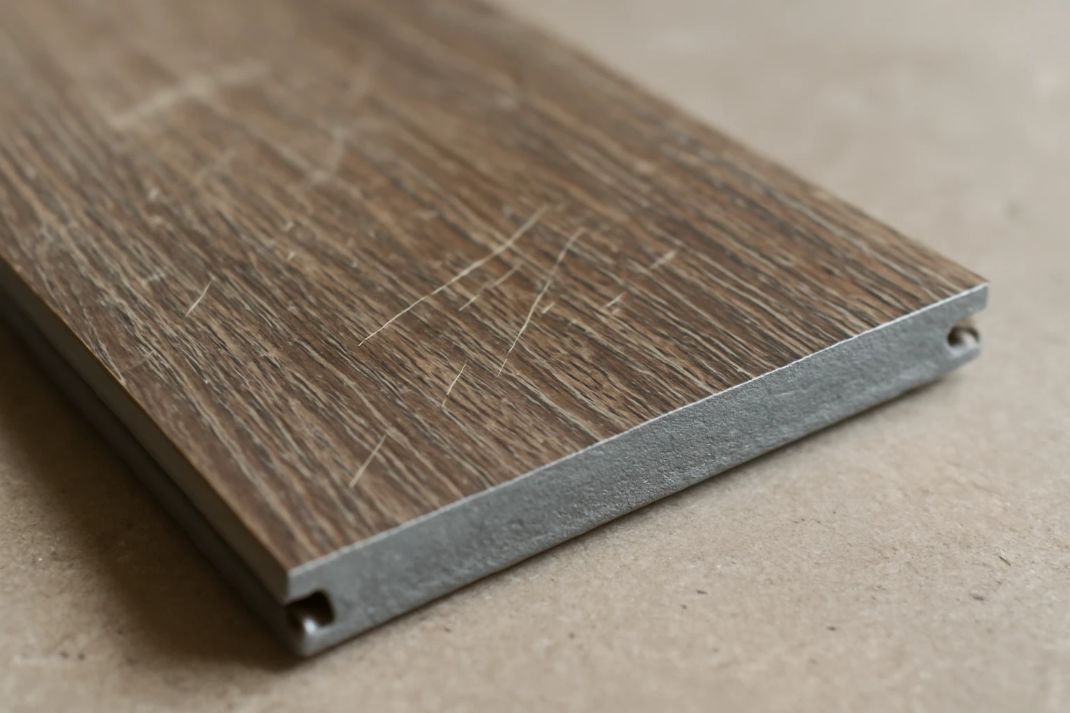 Scratched SPC flooring plank with scuff marks and a cut end exposing the dense gray stone-plastic core, showing a low wear-la